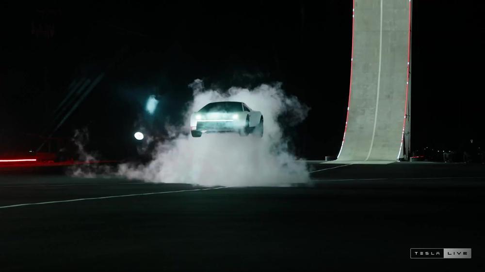 White Tesla Roadster seen from the front in a cloud of smoke next to the curved ramp