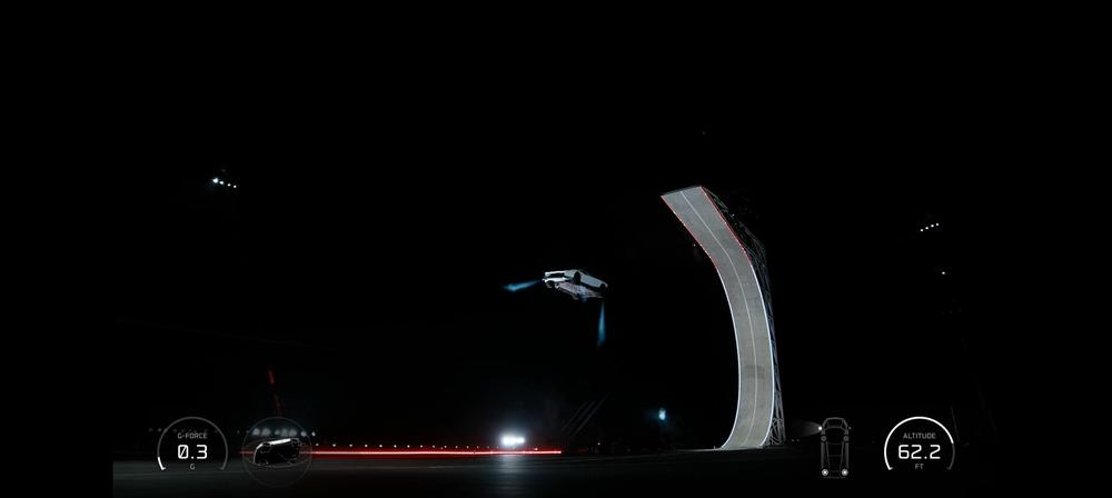 Tesla Roadster in the air next to the curved ramp, thruster jets firing, with the overlay showing 62.2 ft altitude