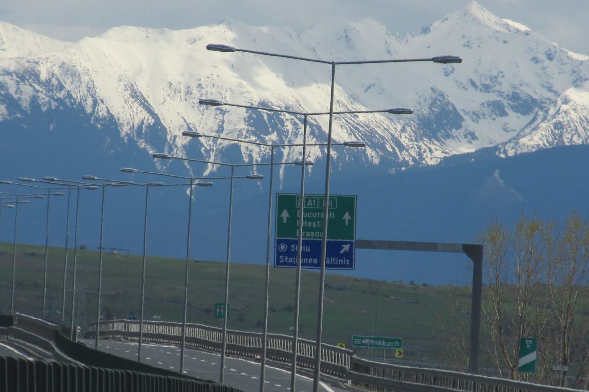 Autostrada A1 pe centura Sibiului, cu Munții Făgăraș înzăpeziți în fundal și indicatoare spre București și Sibiu