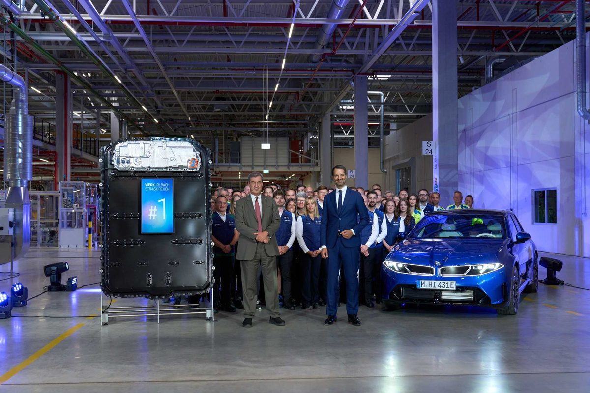 The first series-production battery from Irlbach-Straßkirchen on display next to a blue new BMW i3 and the plant team at the opening ceremony