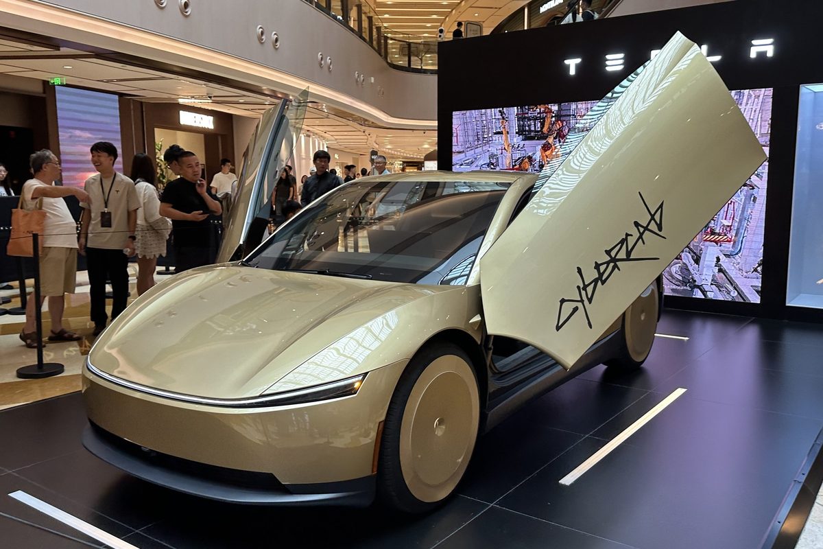 Gold Tesla Cybercab without a steering wheel, displayed with its doors open